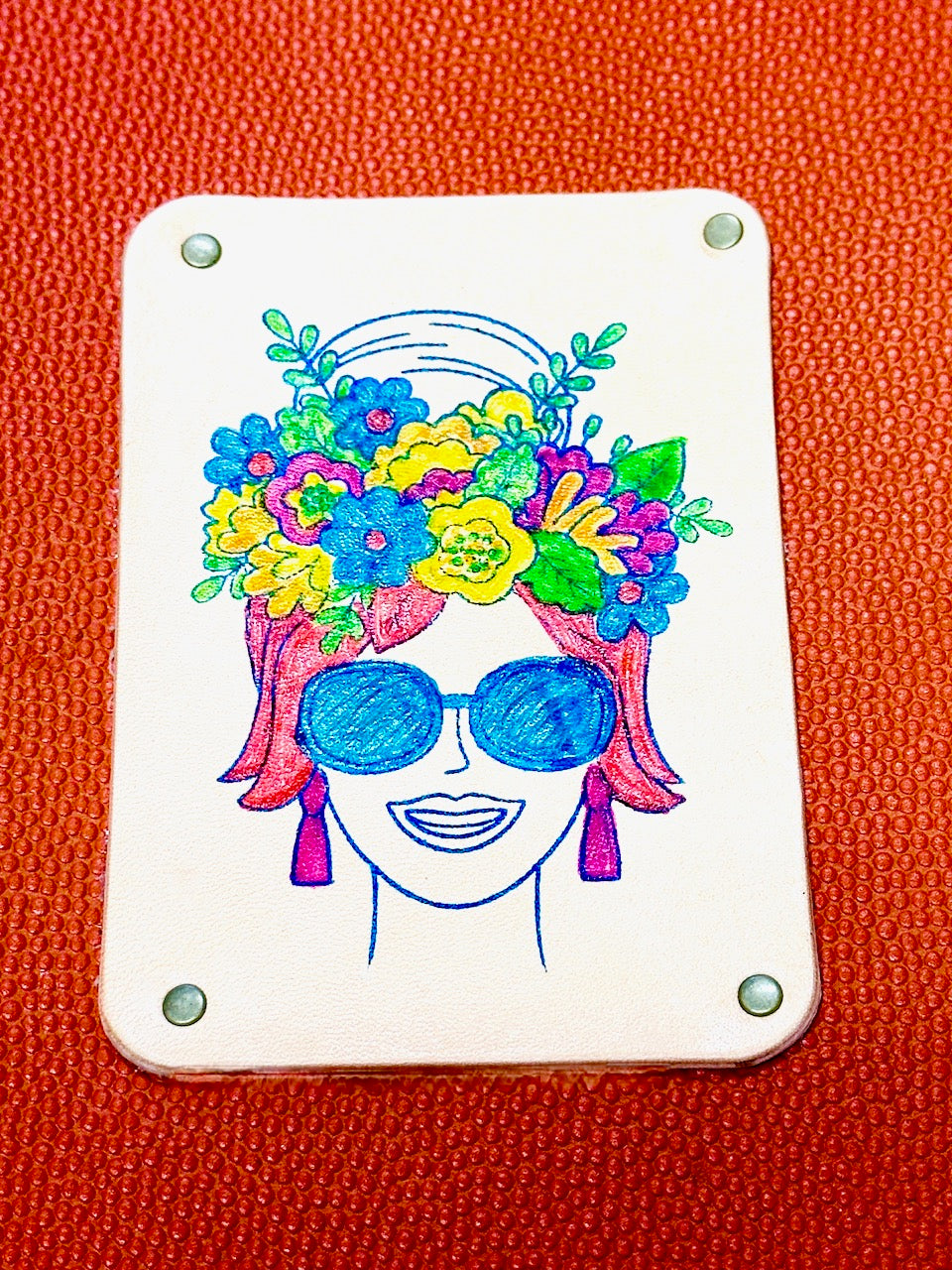 detail of hand painted woman's head with flowers atop orange leather refillable journal by undercover popular leather goods.