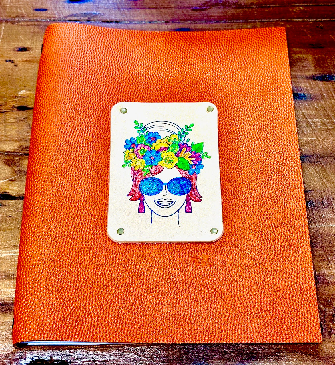 front cover of diva woman on orange leather journal and she has flowers on her head and is wearing sunglasses