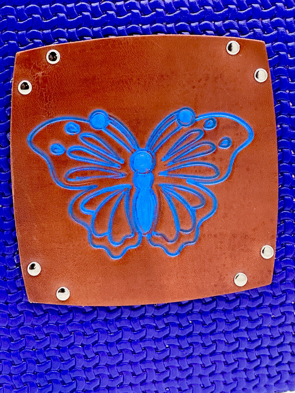 close up of embossed brown leather medallion with a blue inked butterfly image on a blue leather journal